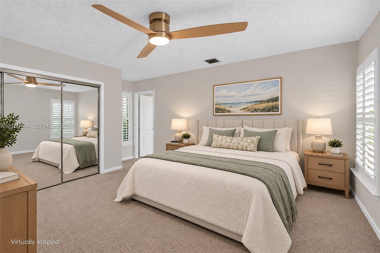 Neutral-toned interior featuring wall-to-wall carpeting, floor-to-ceiling mirrored closet doors, a brushed metal ceiling fan with integrated lighting,
