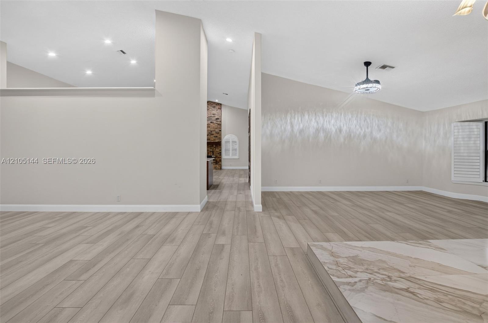 Open-concept interior featuring wood-finish flooring, vaulted ceilings, recessed lighting, and a stone-accented hearth