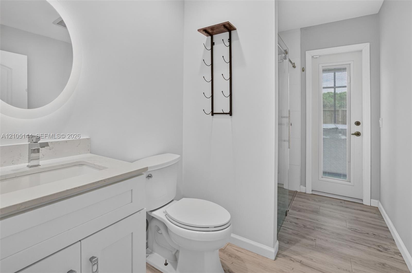 Bathroom featuring a white vanity with a light-toned stone countertop, integrated sink with a chrome faucet, circular LED-backlit mirror, and wood-fin