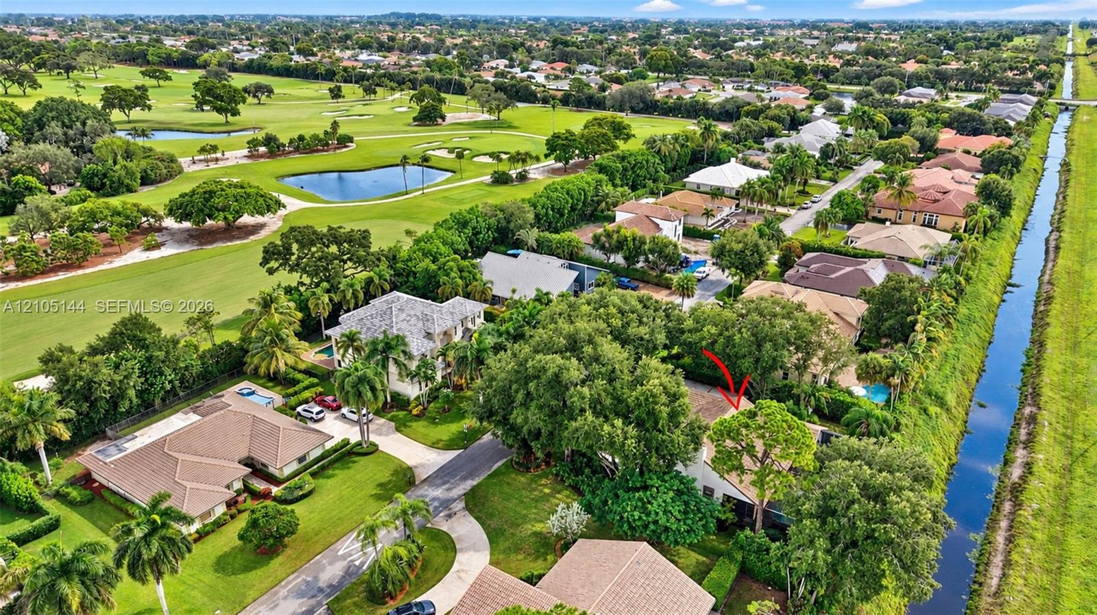 Aerial perspective of property featuring mature canopy trees, tiled roofing, and proximity to canal waterways and golf course grounds