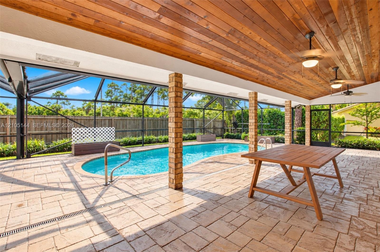 Covered lanai featuring a wood-plank ceiling, brick pillars, and paver flooring, including a screened-in pool with a metal handrail