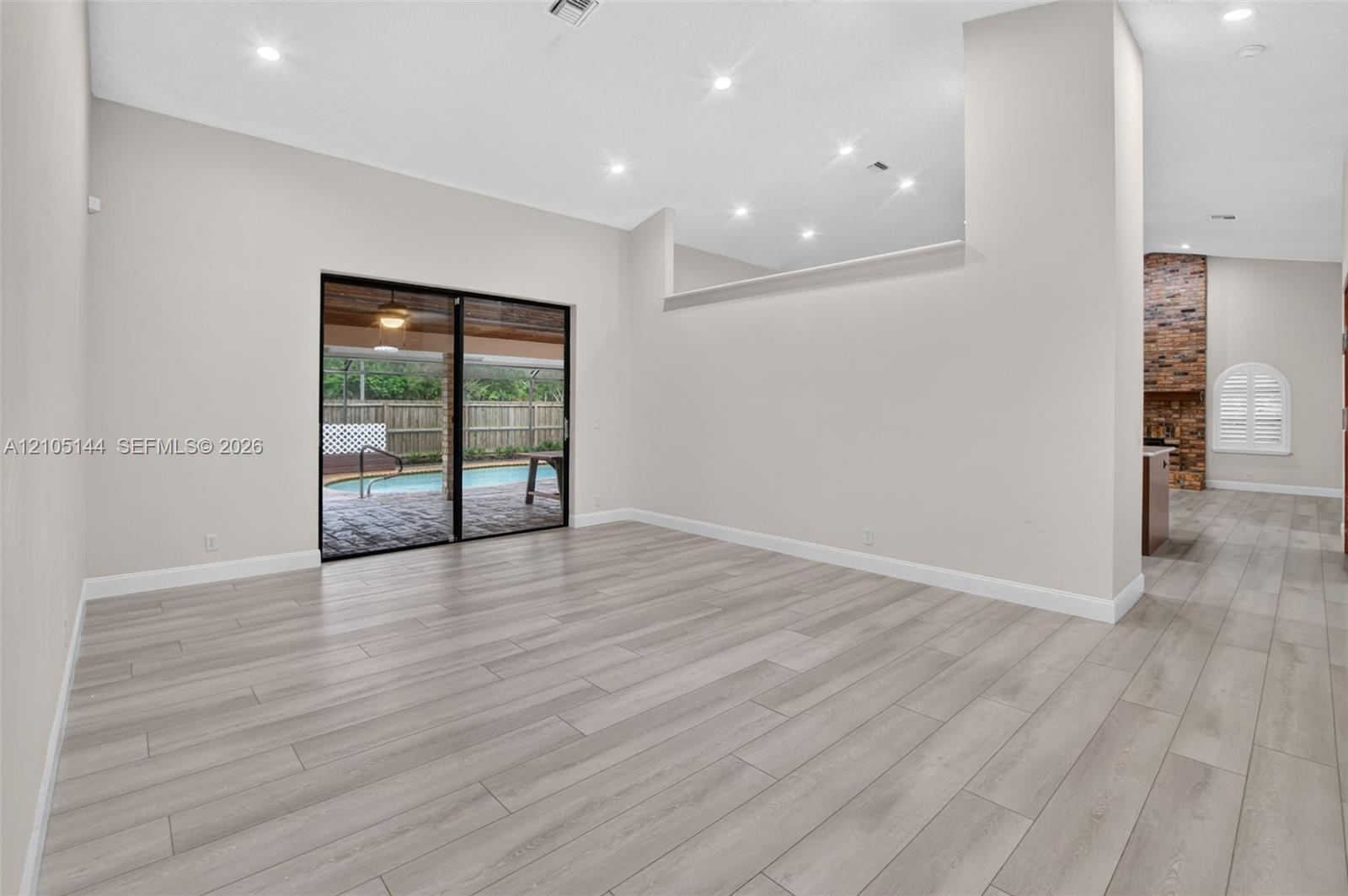 Open living area featuring wood-finish flooring, recessed lighting, high ceilings with architectural cutouts, sliding glass doors, and a brick-accente