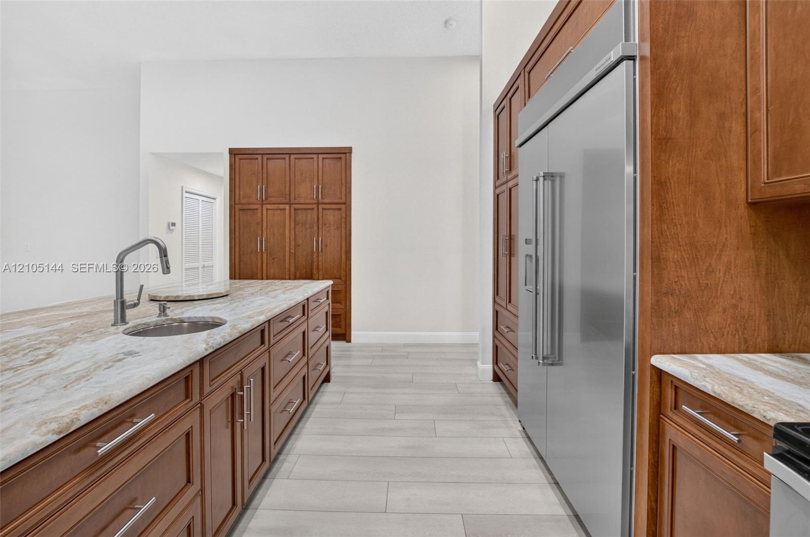 Kitchen featuring wood cabinetry, expansive stone countertops, stainless steel side-by-side refrigerator, under-mount prep sink with high-arc faucet, 