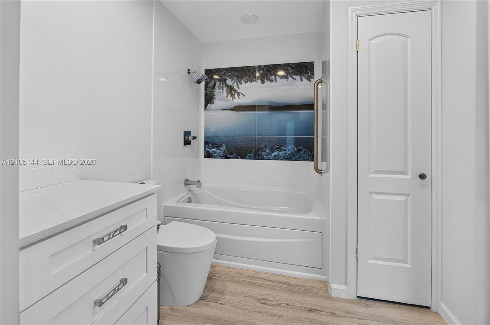 Bathroom featuring white cabinetry with stone-finish countertop, wood-finish flooring, a built-in soaking tub, decorative wall tile inlay, and a wall-