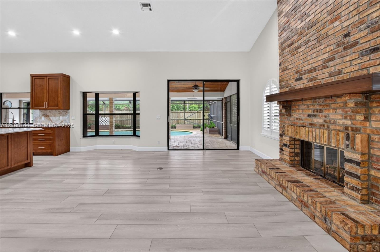 Vaulted ceiling living area featuring a full-height exposed brick fireplace, wood-finish flooring, recessed lighting, and sliding glass doors leading 
