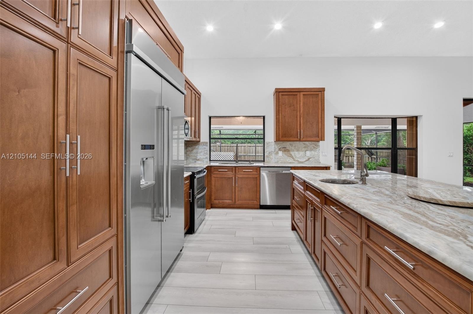 Kitchen featuring wood cabinetry, expansive stone countertops, stainless steel appliances, a center island with a prep sink, and tile flooring