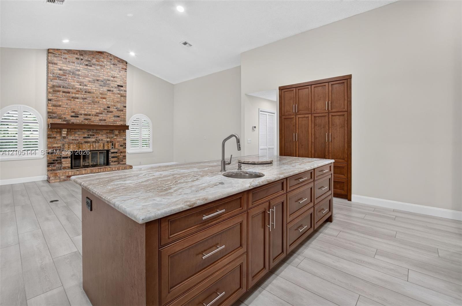 Kitchen island with stone-finish countertop, integrated sink, and wood-finish cabinetry, featuring a full-height pantry, wood-finish flooring, and a b