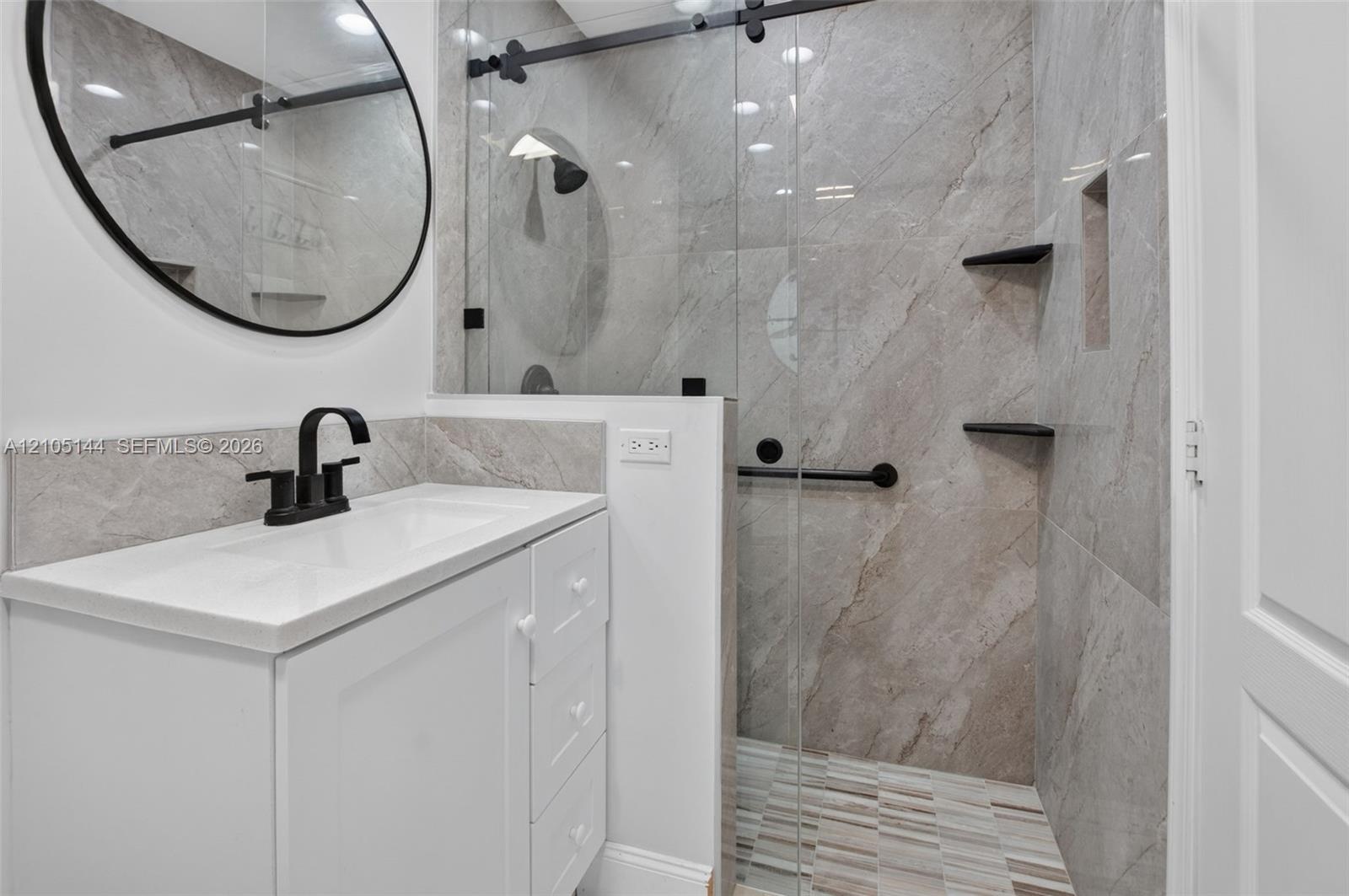 White vanity cabinet with an integrated rectangular sink and matte black faucet, paired with a frameless glass shower enclosure featuring large-format
