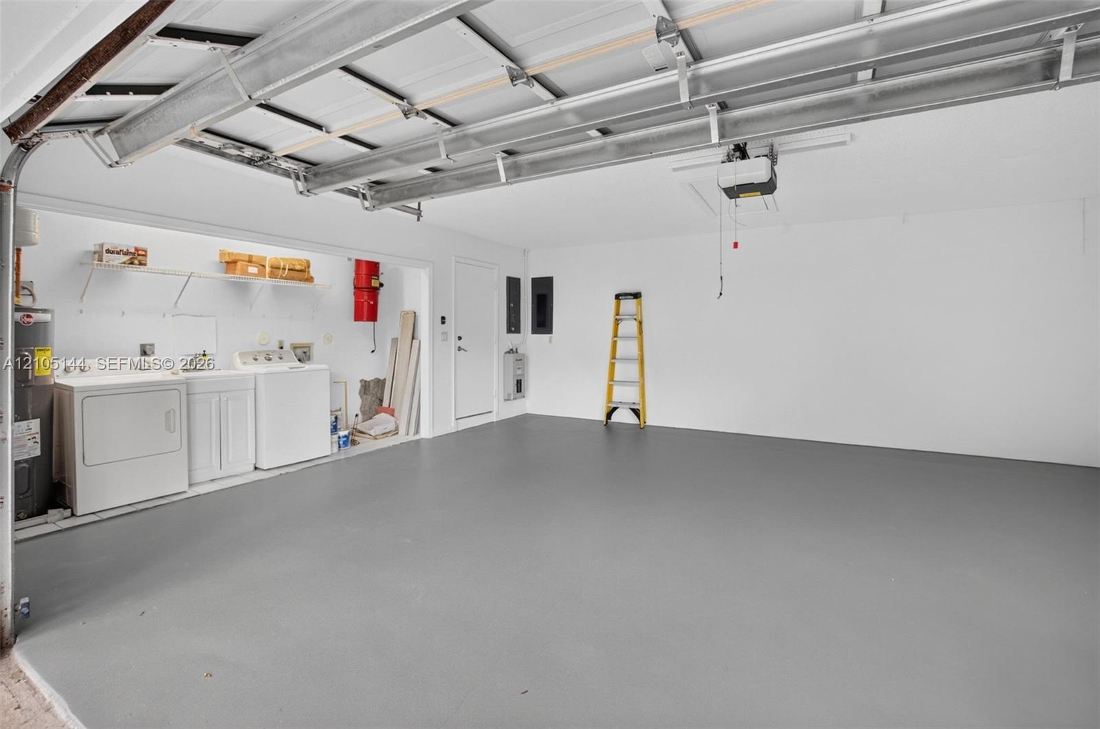 Garage space featuring a smooth epoxy-finish floor, built-in laundry area with utility sink, ceiling-mounted automatic door opener, and white wall fin