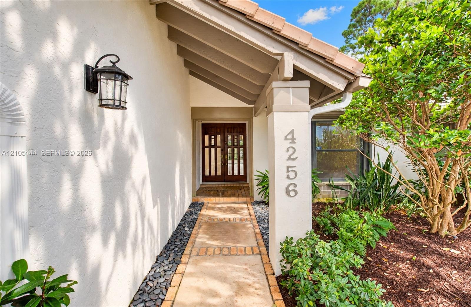 Covered entryway featuring a concrete paver walkway, stucco exterior, decorative wall-mounted light fixture, and double entry doors with vertical glas