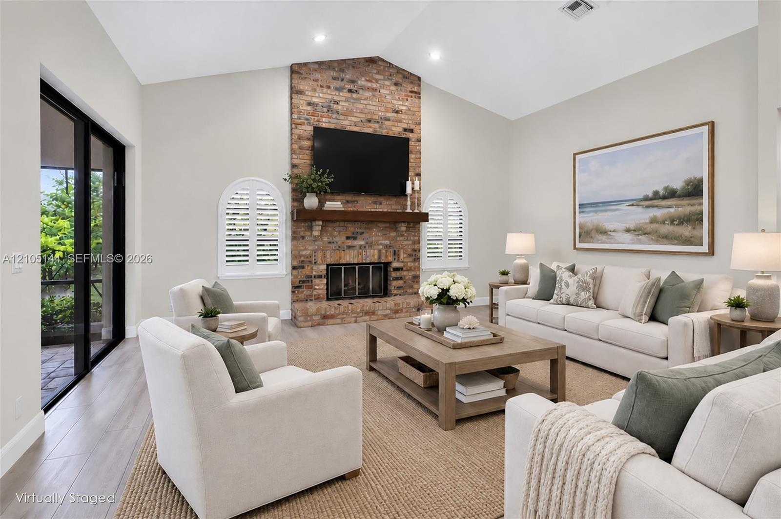 Living area featuring a floor-to-ceiling brick fireplace, natural wood mantel, vaulted ceilings, arched windows with plantation shutters, and wood-fin