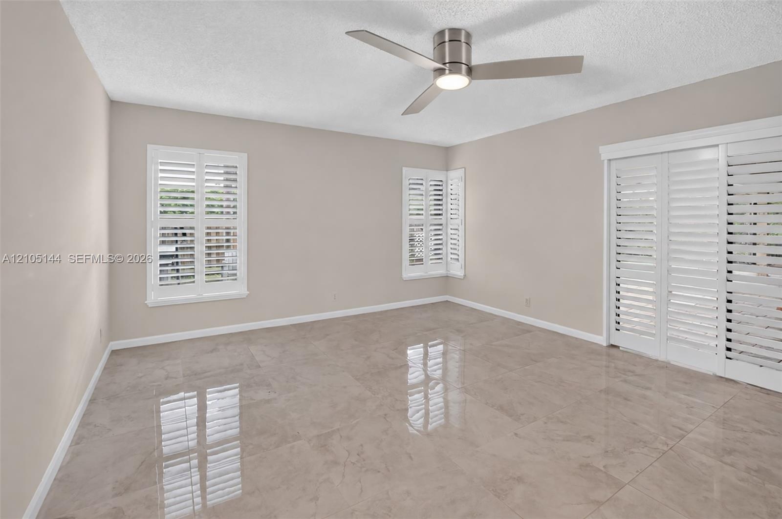 (FAN VIRTUALLY STAGED AS SIMILAR PIECE WILL BE INSTALLED)Large-format neutral tile flooring, triple white plantation shutters, and a modern brushed-ni
