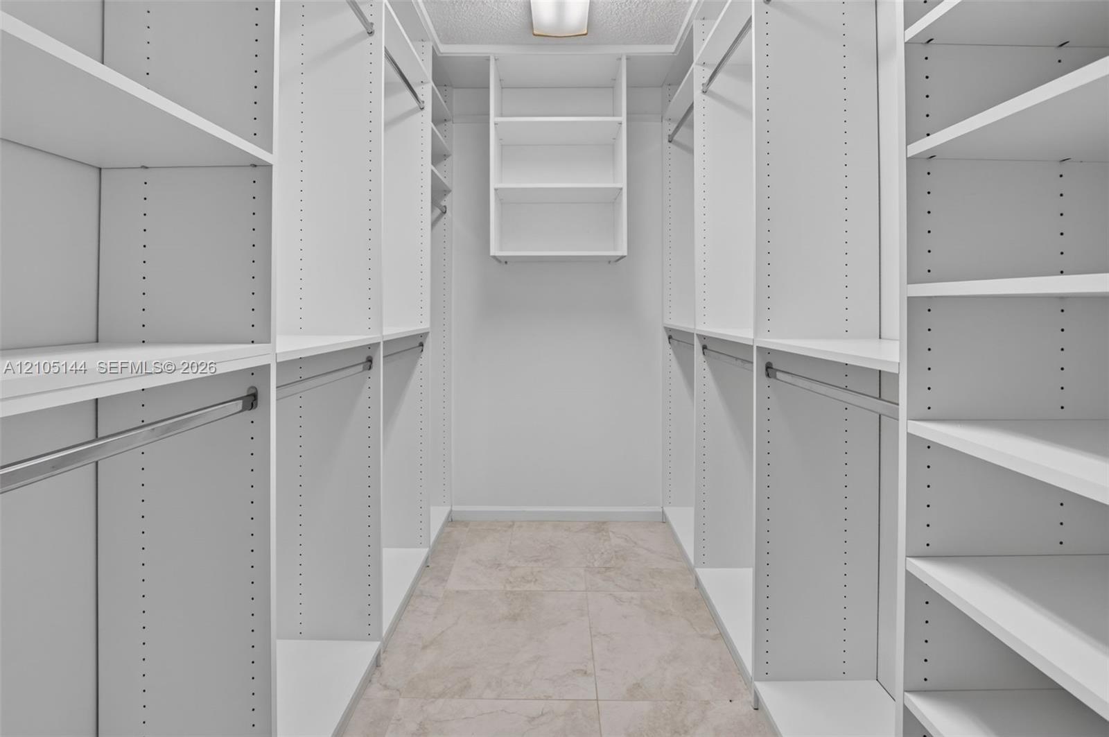 Walk-in closet featuring white built-in shelving, adjustable shelf tracks, metal garment rods, and tile flooring
