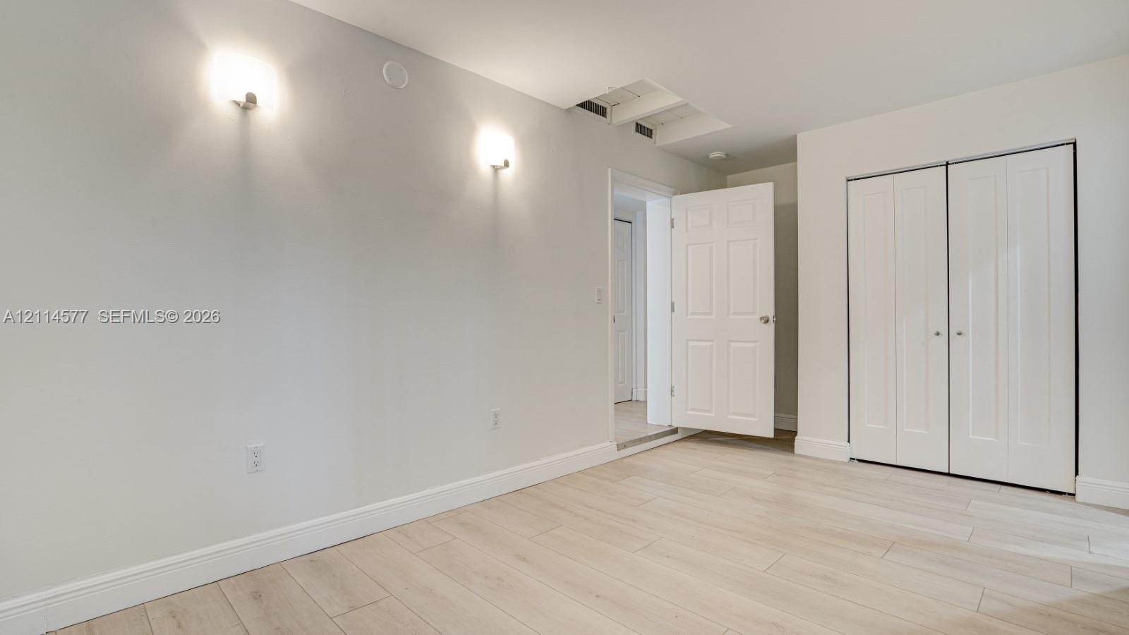 Interior space featuring light-toned wood-finish flooring, neutral walls, two wall-mounted light fixtures, and a white six-panel closet door