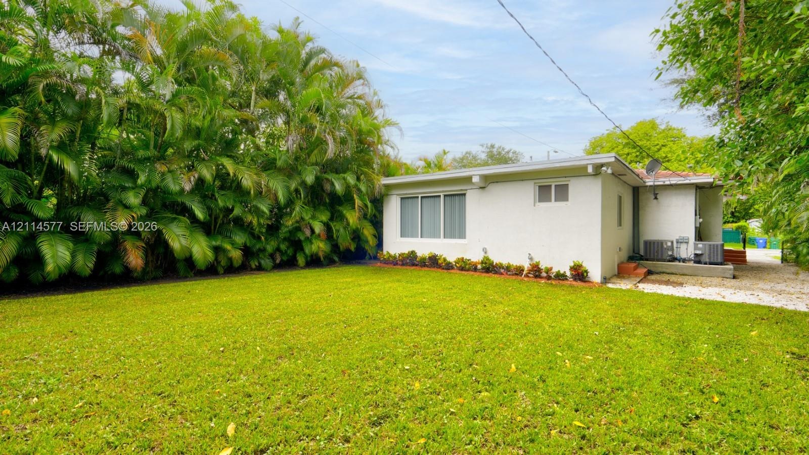 Expansive lawn area featuring mature perimeter palm trees, painted brick exterior, and multi-pane window configuration
