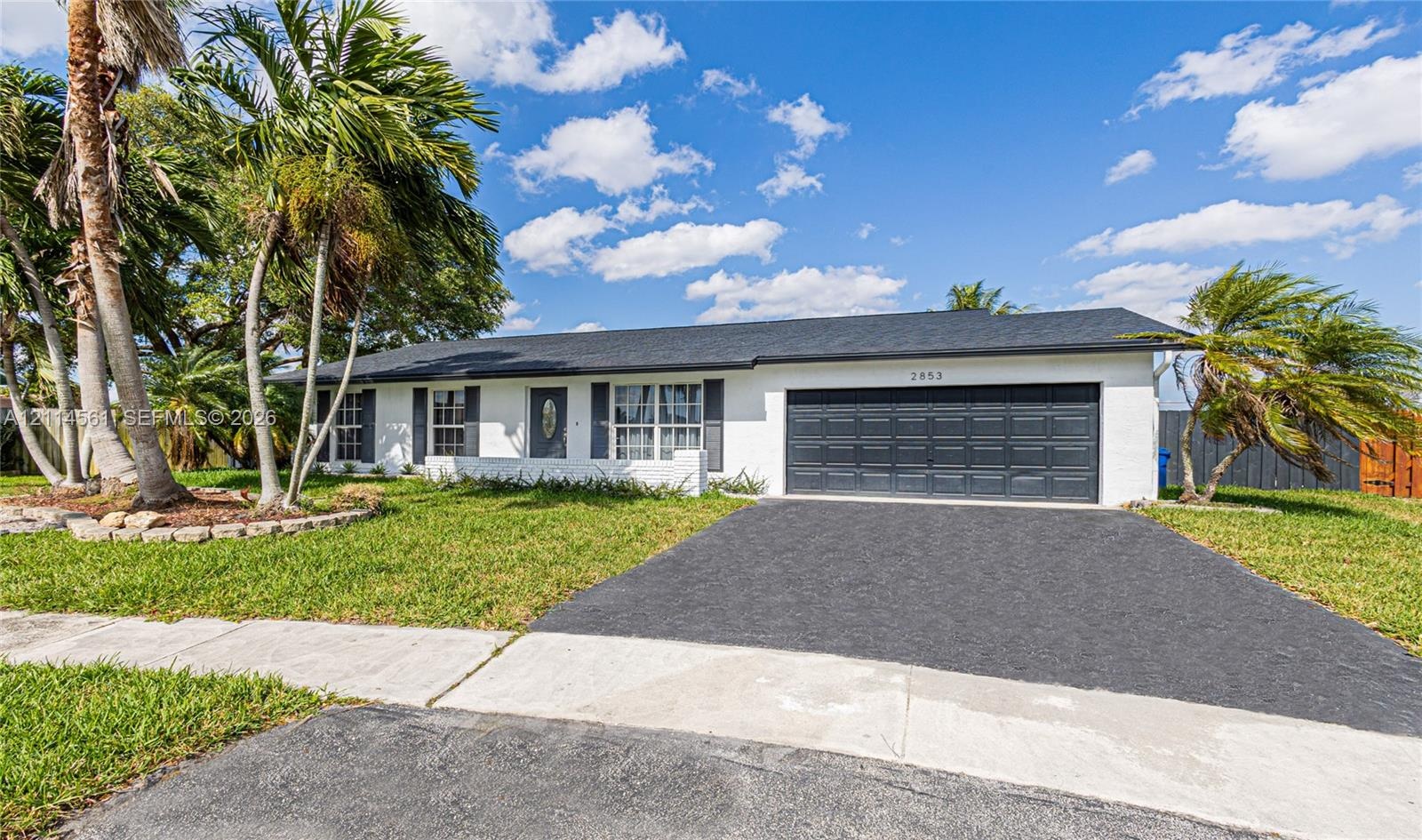 Single-story exterior featuring white stucco siding, a dark-toned asphalt shingle roof, a two-car garage, and shuttered windows