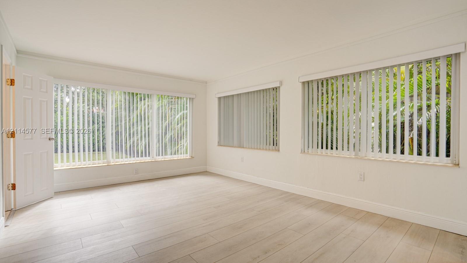 Interior space featuring wood-finish flooring, multi-pane windows with vertical blinds, and a paneled entry door