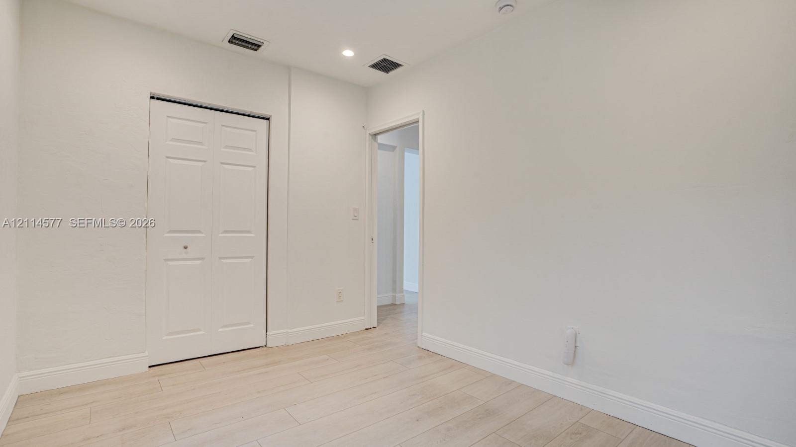 Interior space featuring wood-finish flooring, white walls, and a closet with bifold doors