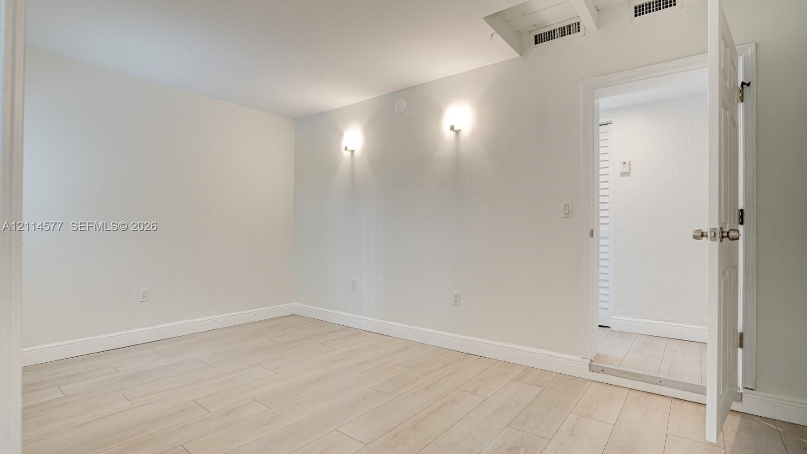 Neutral interior space featuring wood-finish flooring, dual wall-mounted light fixtures, and a six-panel interior door