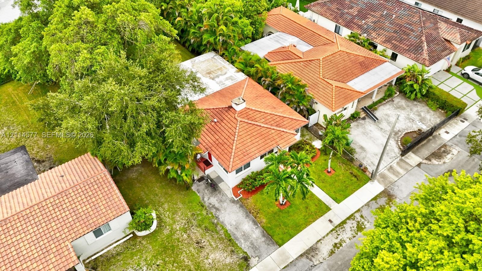 Aerial perspective of a property featuring a clay tile roof, concrete driveway, manicured lawn, and mature landscaping