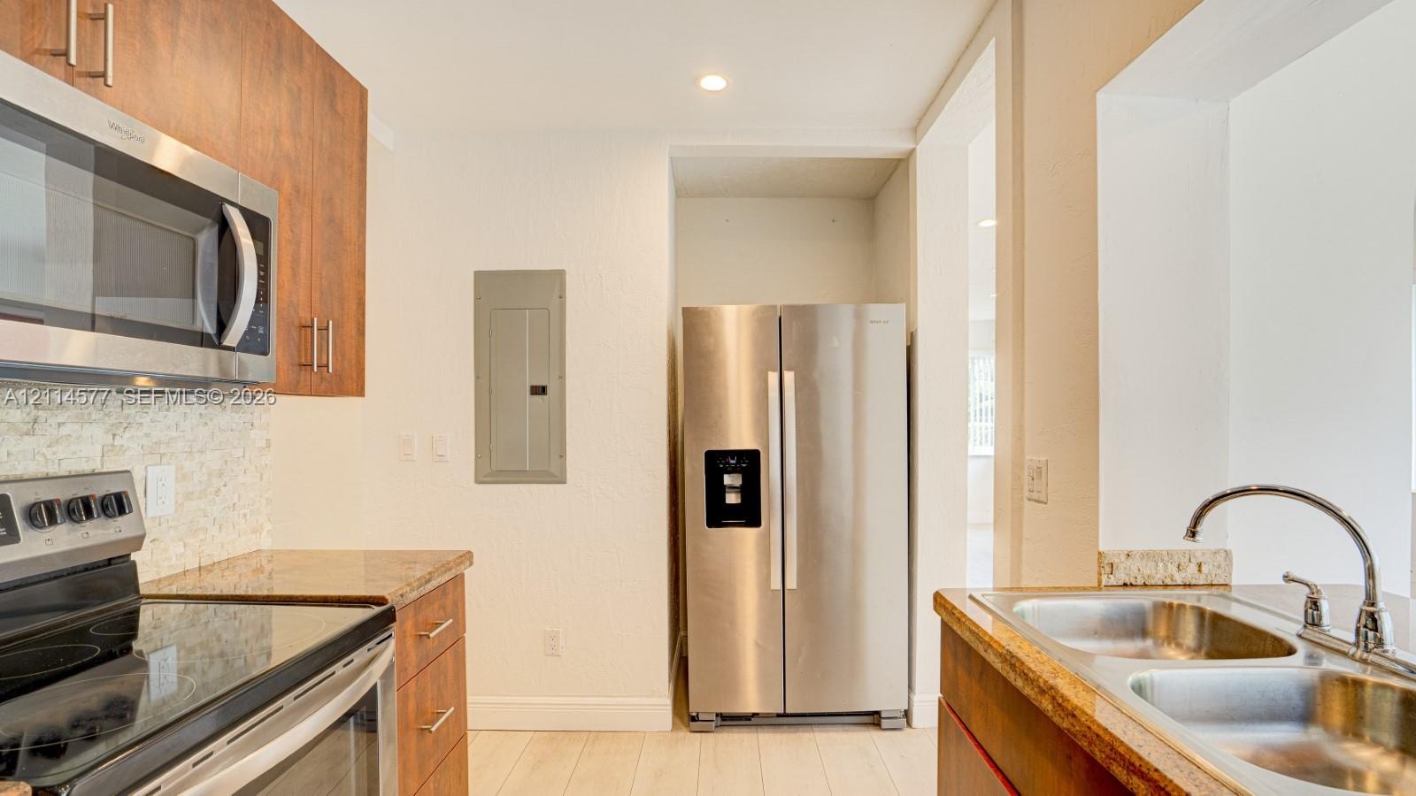 Kitchen featuring flat-panel wood-finish cabinetry, stainless steel appliances, stone countertops, textured stone tile backsplash, and a double-basin 