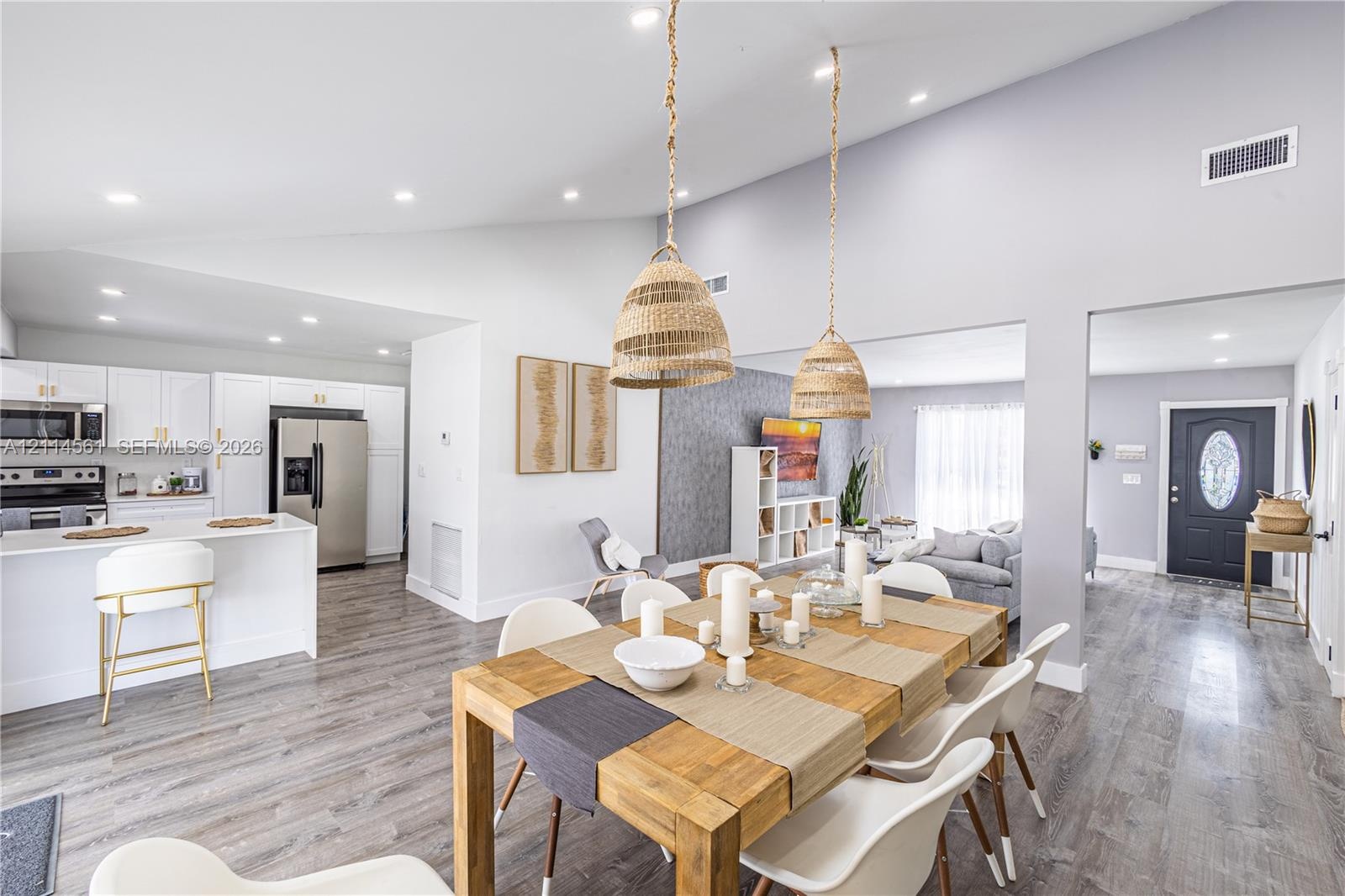 Vaulted ceilings, open-concept kitchen with white cabinetry and stainless steel appliances, wood-finish flooring, and natural-textured pendant lightin