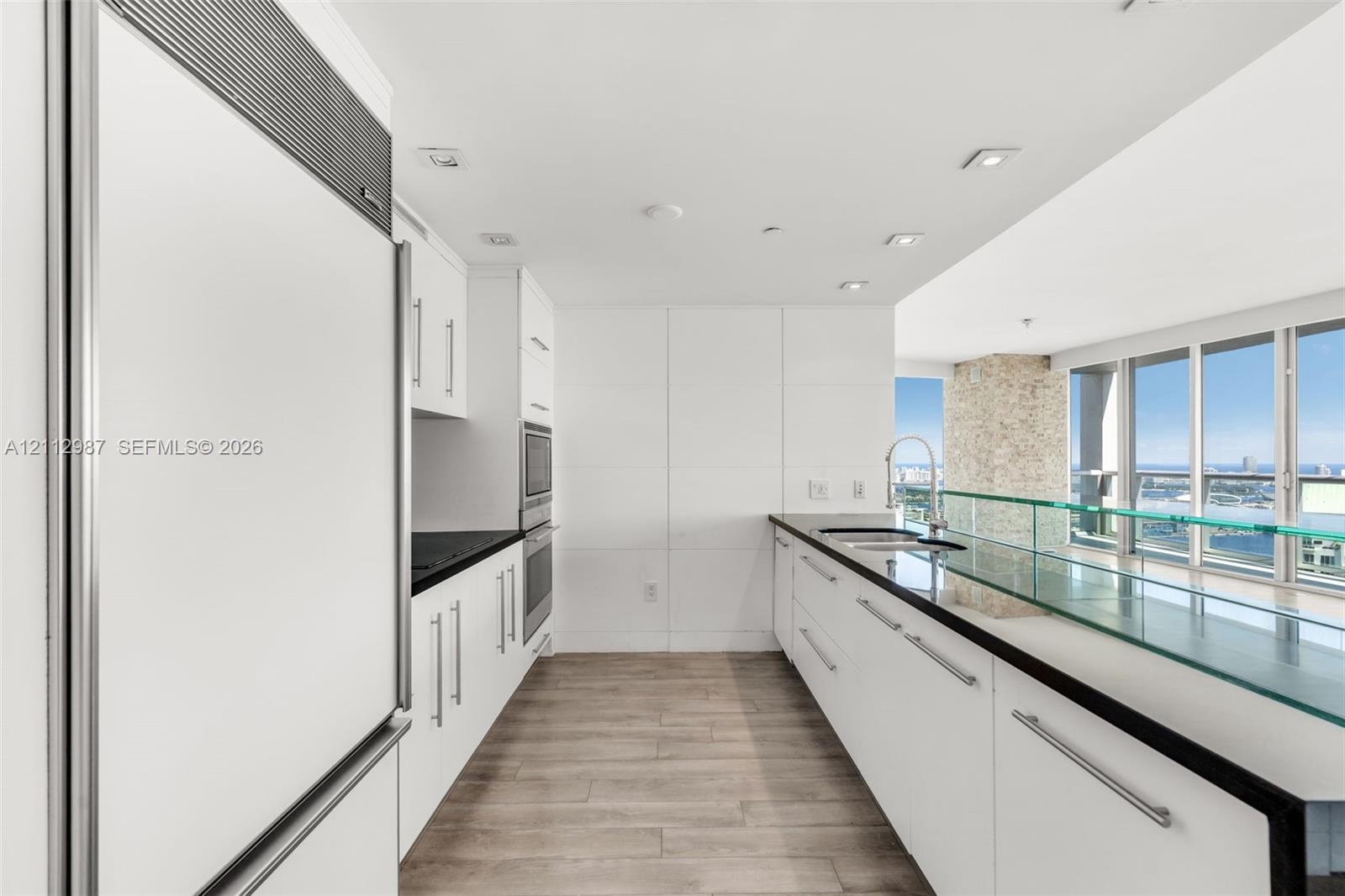Kitchen featuring white flat-panel cabinetry, dark countertops, a glass-topped breakfast bar, integrated appliances, and wood-finish flooring