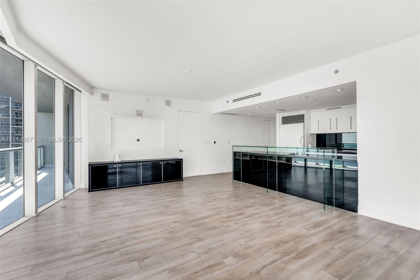 Open-concept floor plan featuring wood-finish flooring, floor-to-ceiling glass wall, built-in black lacquer cabinetry, and a kitchen island with a gla