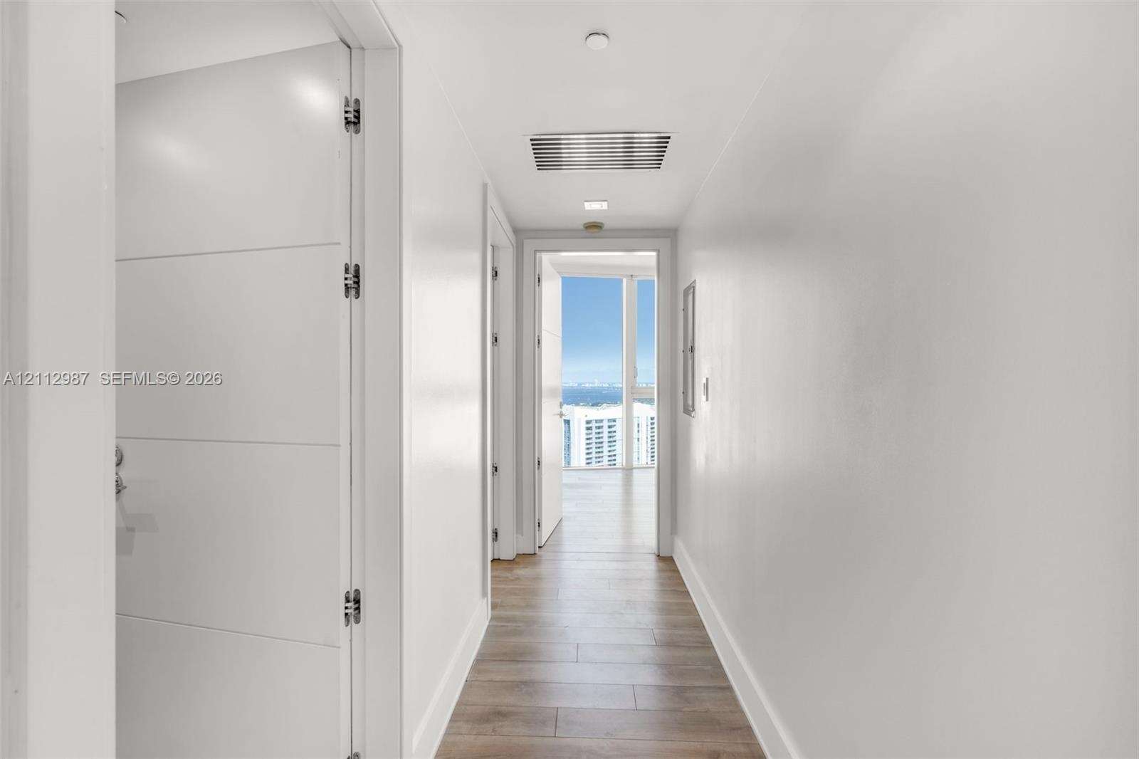 Hallway featuring horizontal-panel interior doors, light wood-finish flooring, and floor-to-ceiling windows with coastal scenery