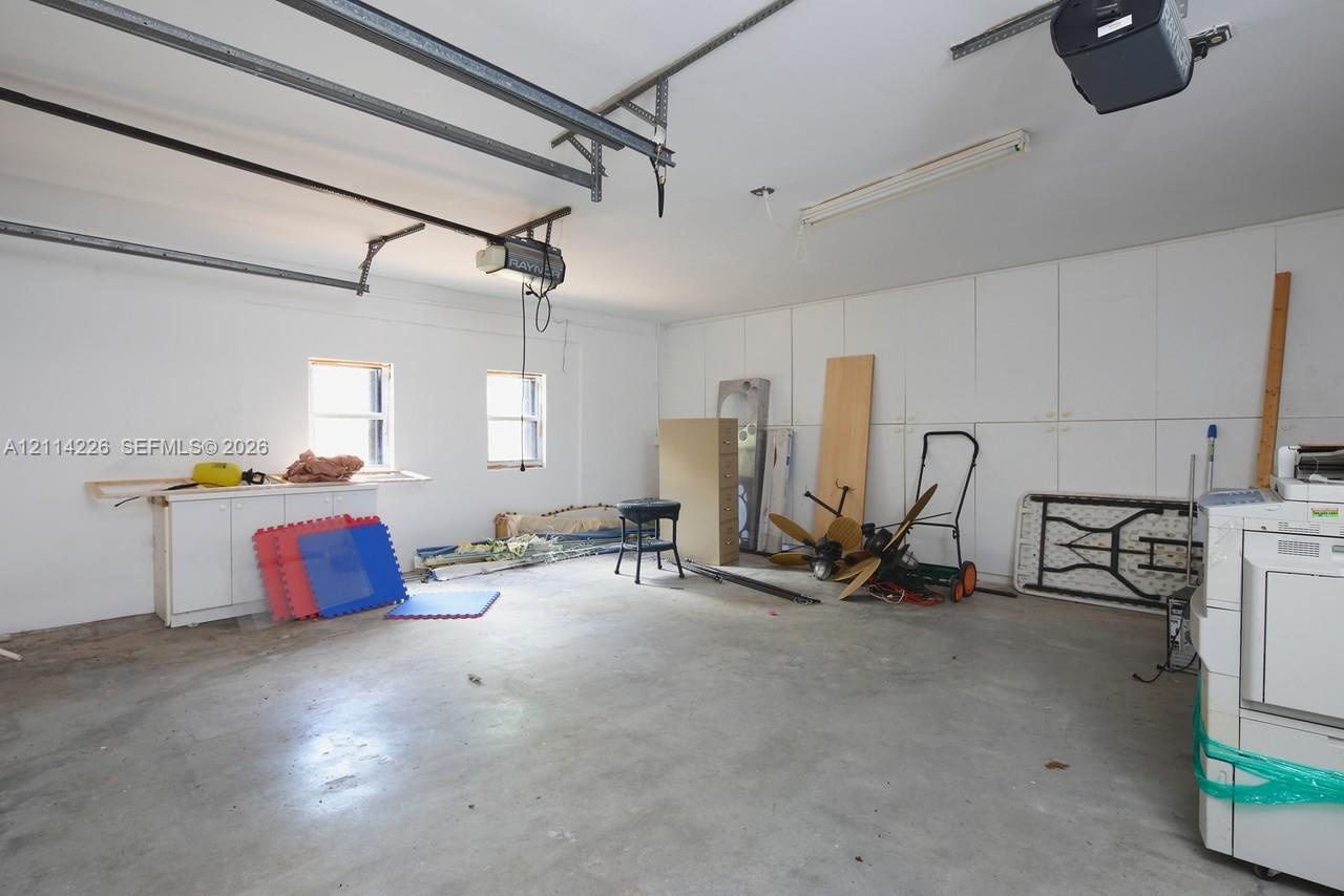 Attached garage featuring white built-in cabinetry, dual wall-mounted garage door openers, fluorescent lighting, and two windows