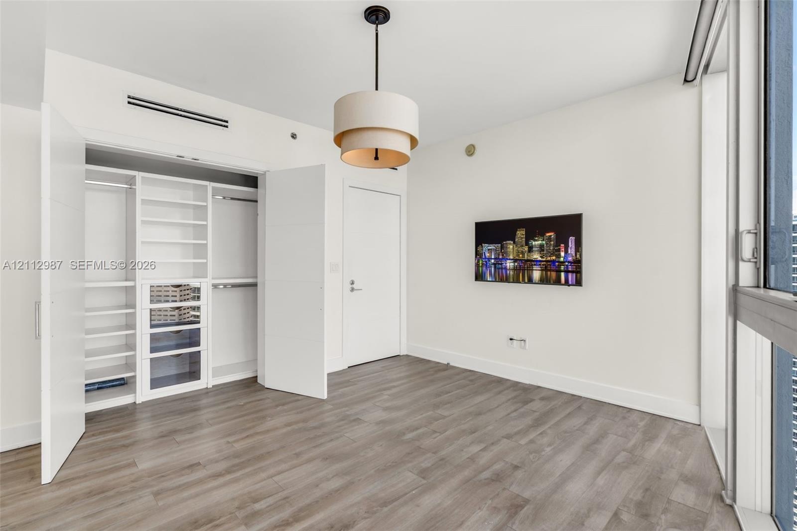 Wood-finish flooring, custom built-in closet system with integrated shelving and drawers, tiered drum pendant lighting, and floor-to-ceiling glass pan