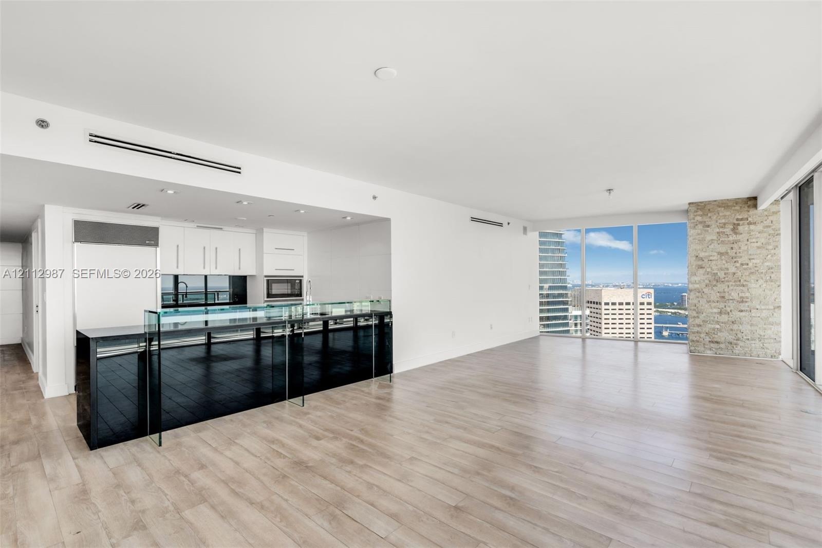 Open-concept kitchen featuring a black stone island with a glass breakfast bar, white cabinetry, integrated stainless steel appliances, wood-finish fl