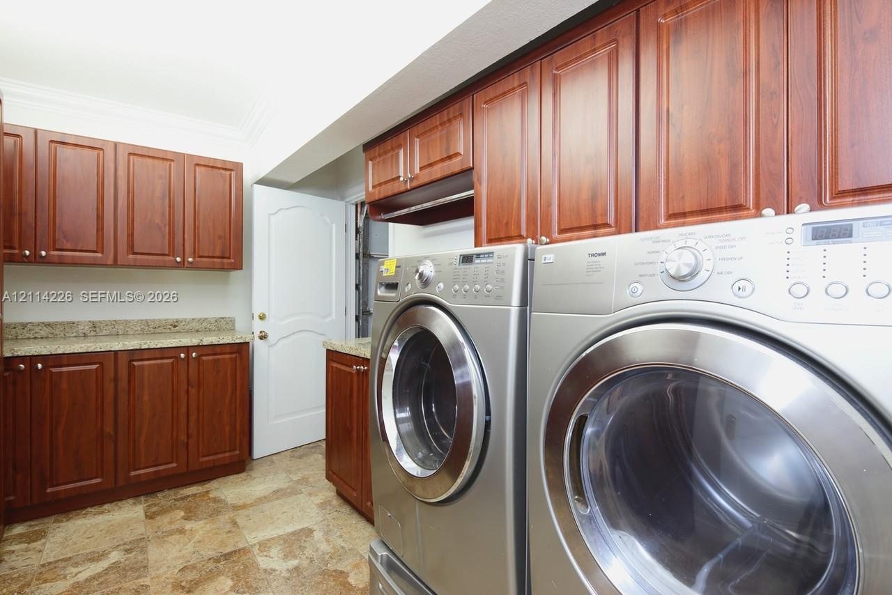Laundry room featuring raised-panel wood cabinetry, stone-finish countertops, tile flooring, and crown molding