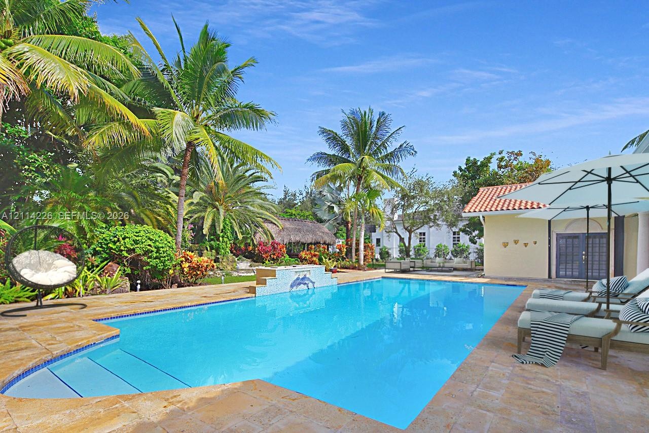 In-ground swimming pool featuring a tiled mosaic water feature, expansive stone-paver decking, and surrounding mature tropical landscaping