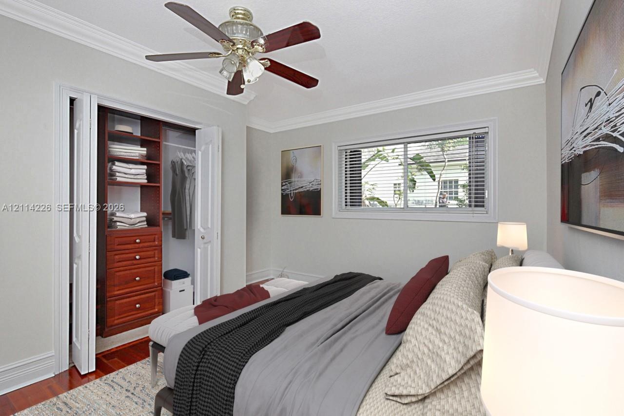 Wood-finish flooring, crown molding, built-in wooden closet cabinetry, and a ceiling fan with integrated lighting