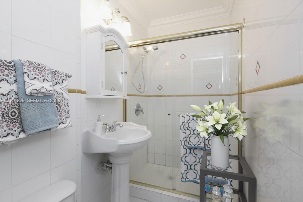 Pedestal sink, wall-mounted medicine cabinet, white tile surround with decorative inlays, and glass-enclosed shower featuring a handheld fixture