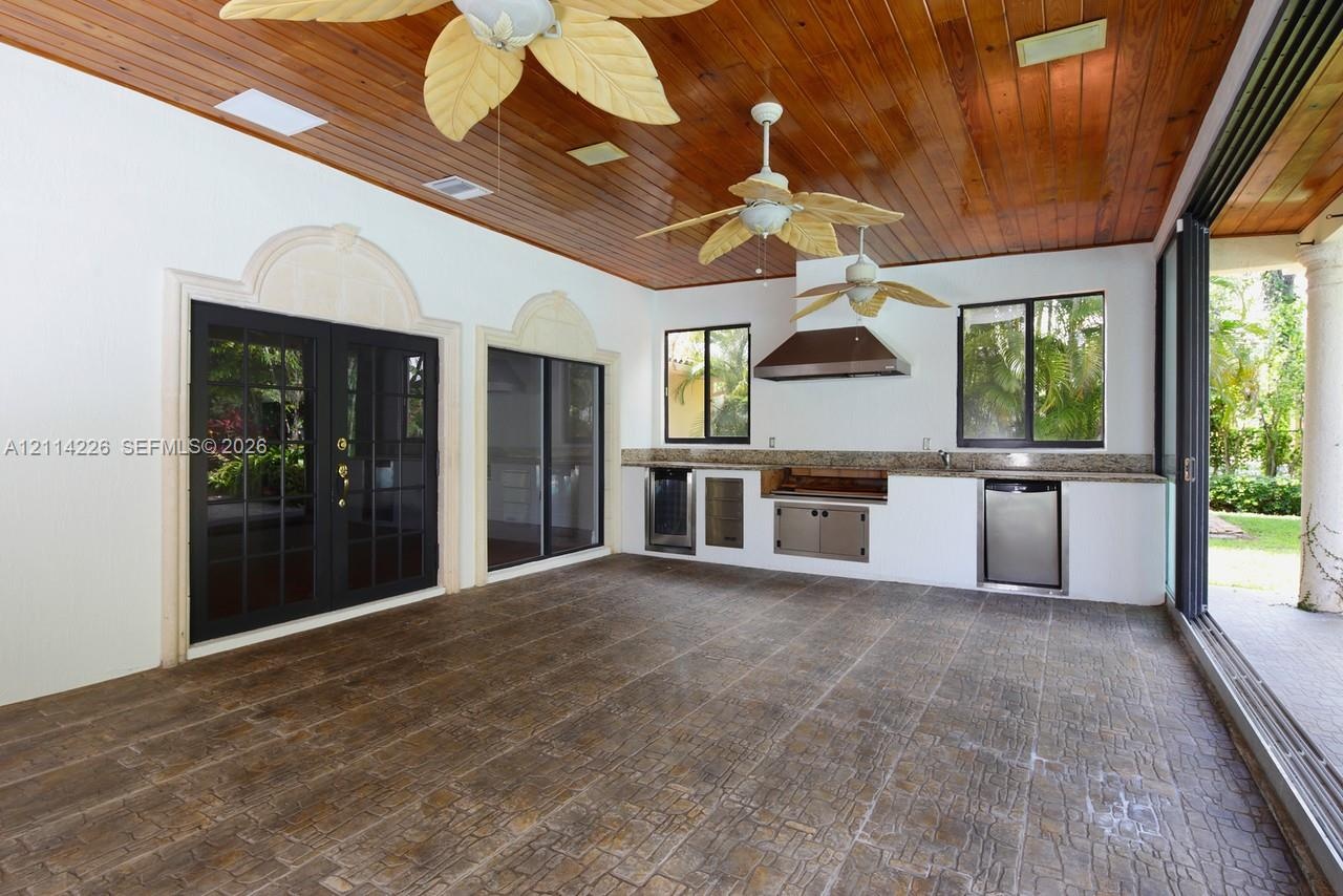 Covered outdoor living space featuring a wood-plank ceiling, ceiling fans, stone-finish tile flooring, and a built-in outdoor kitchen with stainless s