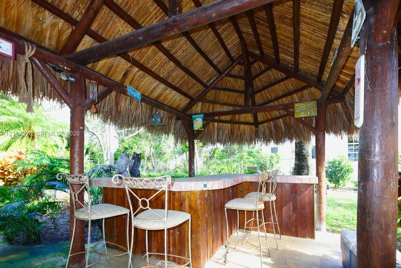Outdoor palapa featuring a thatched roof, exposed timber support beams, and a built-in bar with wood-panel base and brick-trim countertop