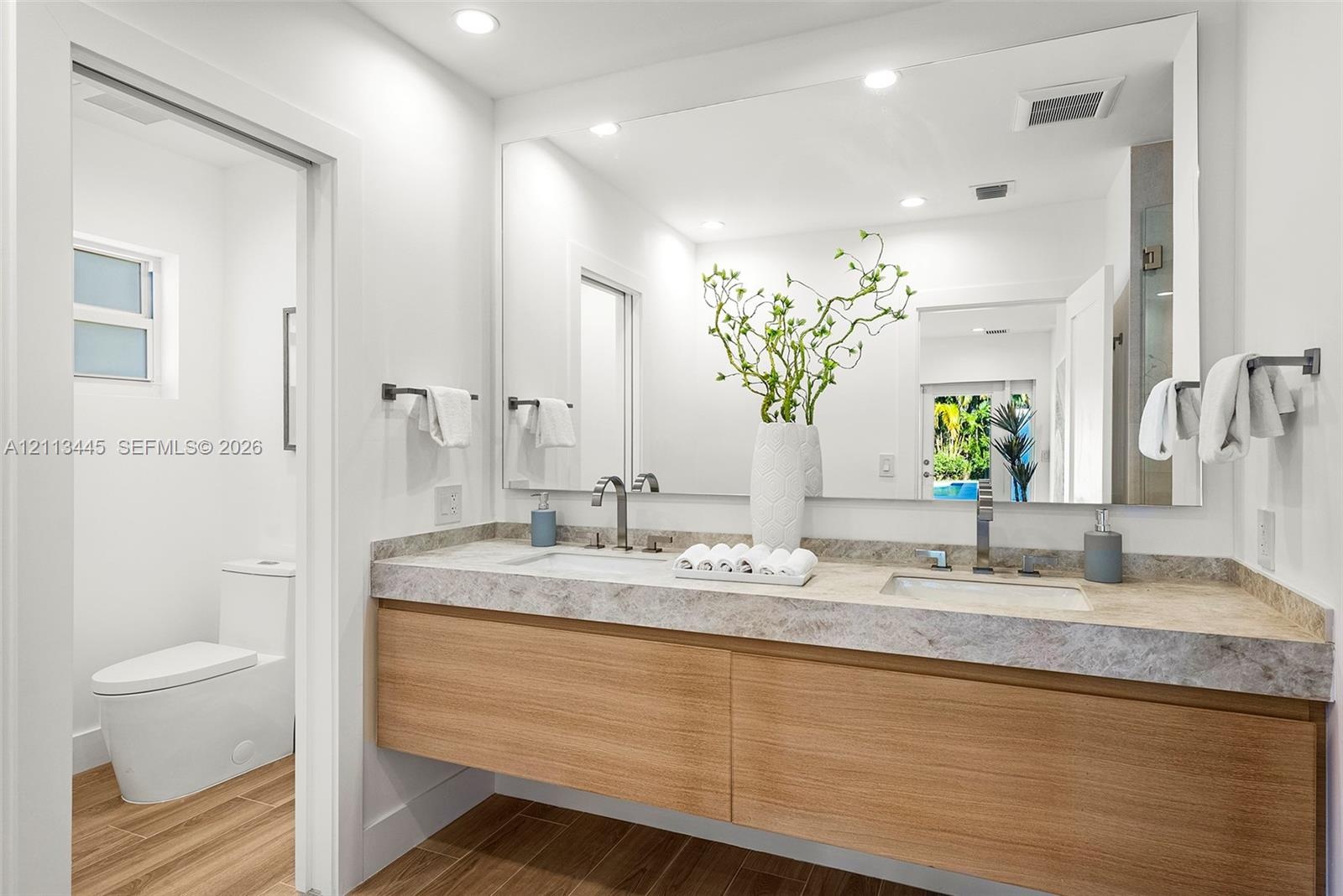 Floating wood-finish vanity with dual integrated sinks, stone-finish countertop, full-width vanity mirror, and wood-finish flooring