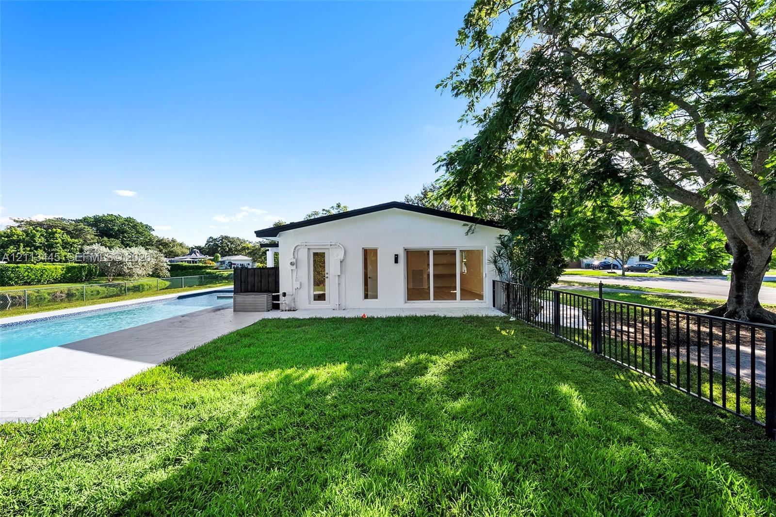 Exterior rear elevation featuring white stucco siding, a rectangular swimming pool with paved surround, expansive manicured lawn, and black metal peri