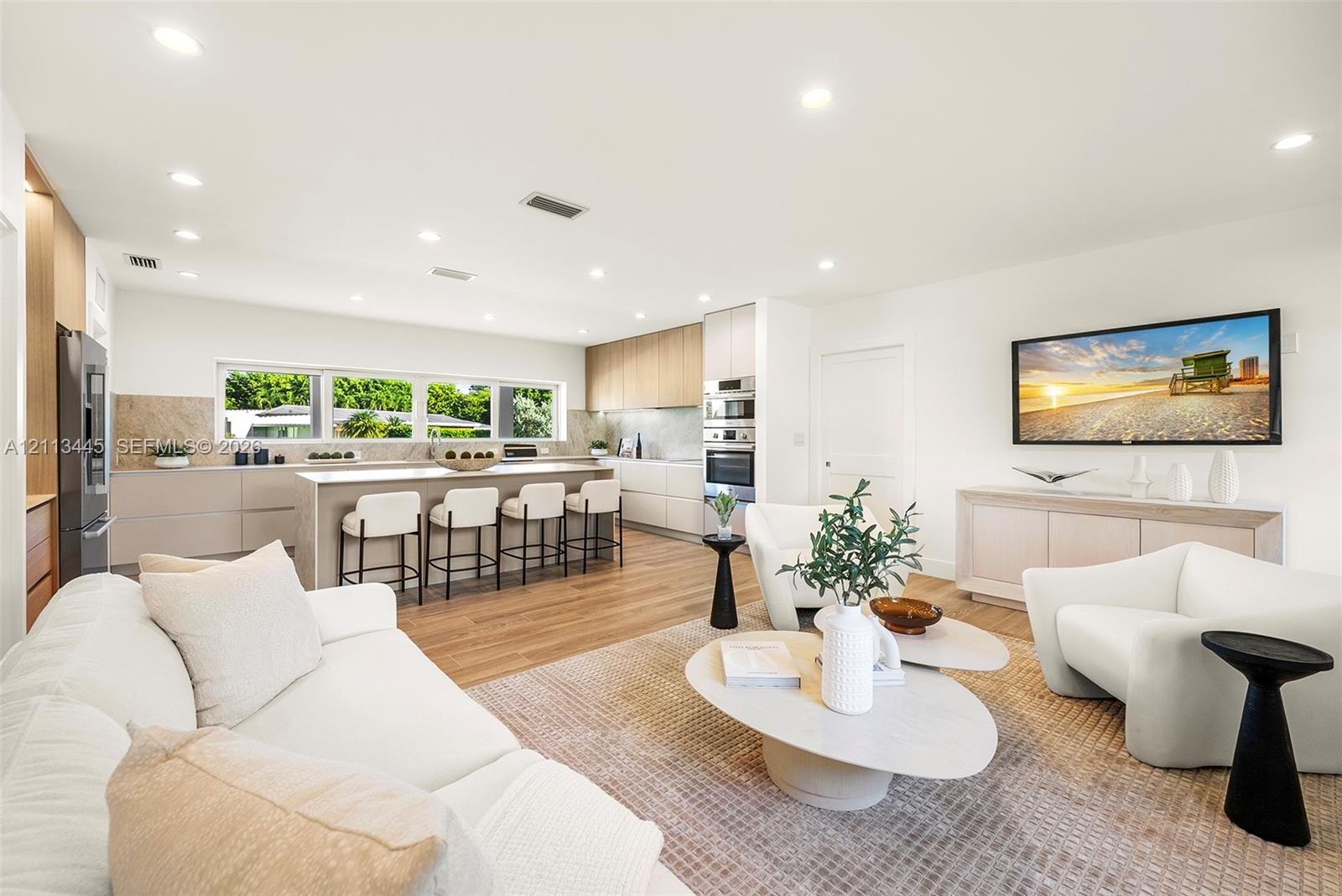 Open-concept living space featuring wood-finish flooring, recessed lighting, a central island with stone-finish countertops, handleless cabinetry, and