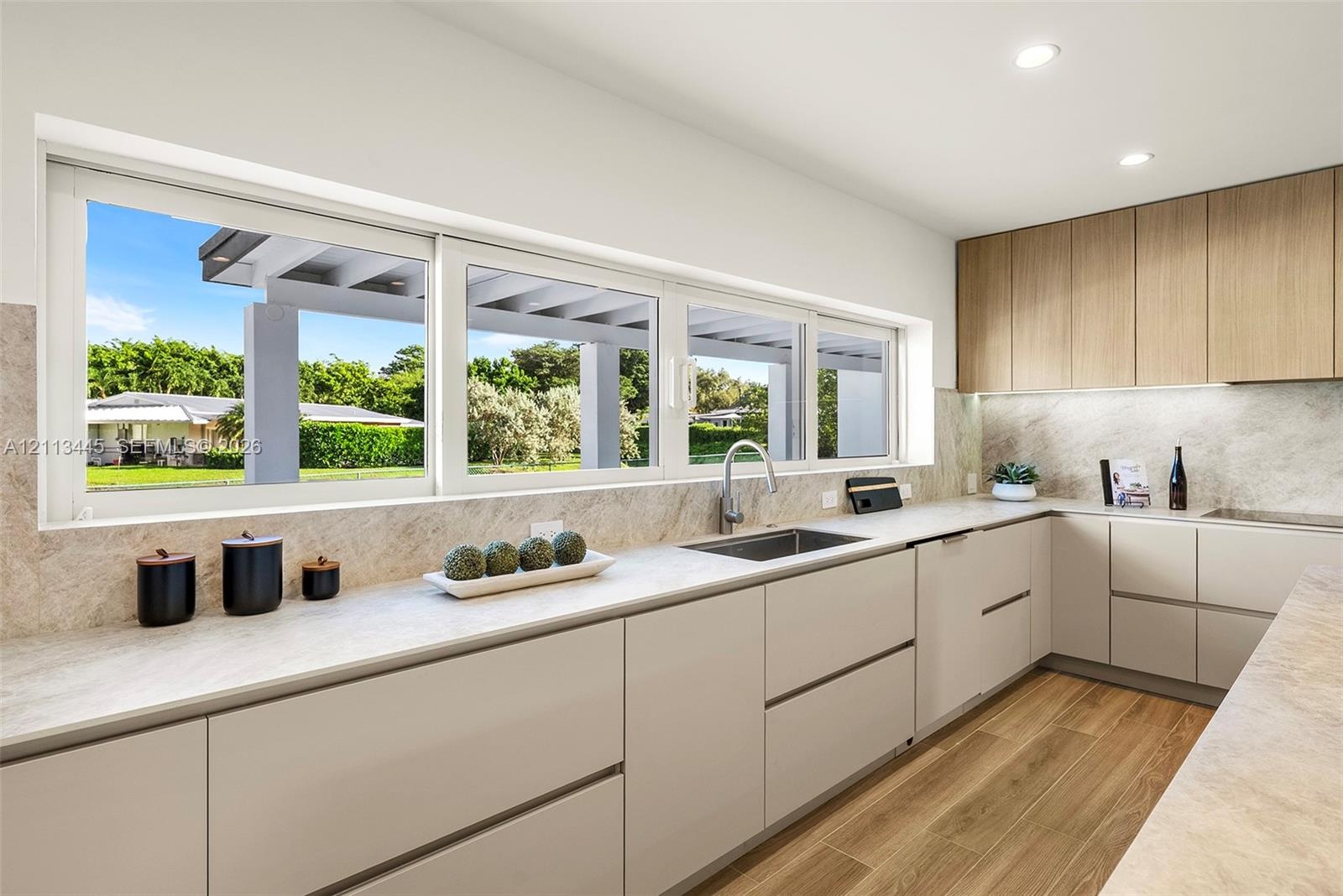 Modern kitchen featuring light-toned cabinetry, wood-finish flooring, stone-textured countertops and backsplash, and an integrated undermount sink wit