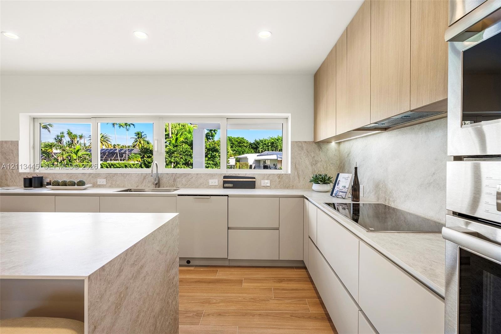Kitchen featuring flat-panel cabinetry, wood-finish flooring, stone-finish countertops and backsplash, integrated stainless steel appliances, and a ho