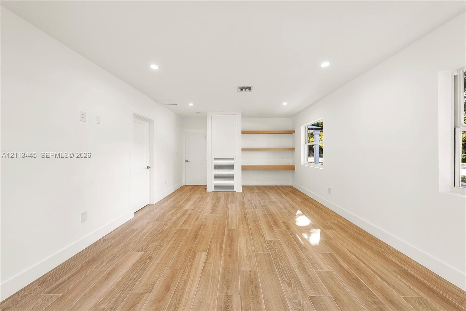 Neutral interior space featuring wood-finish flooring, recessed lighting, and built-in wall shelving