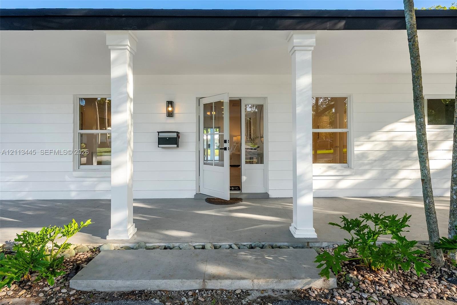 Covered front porch featuring white horizontal siding, square columns, a concrete foundation, and a glass-paneled entry door