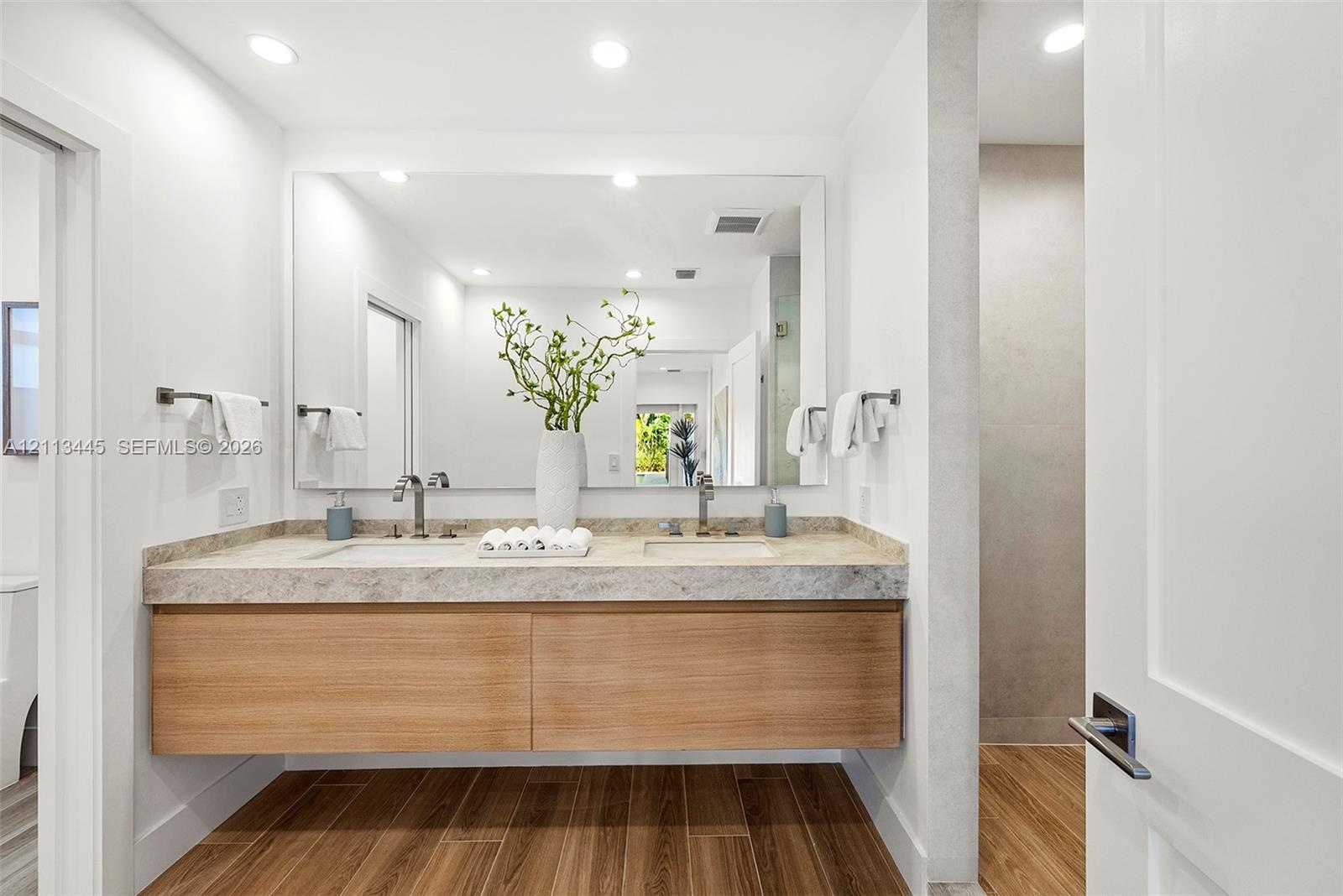 Floating vanity featuring wood-finish cabinetry, dual undermount sinks, stone countertop, and full-width wall mirror