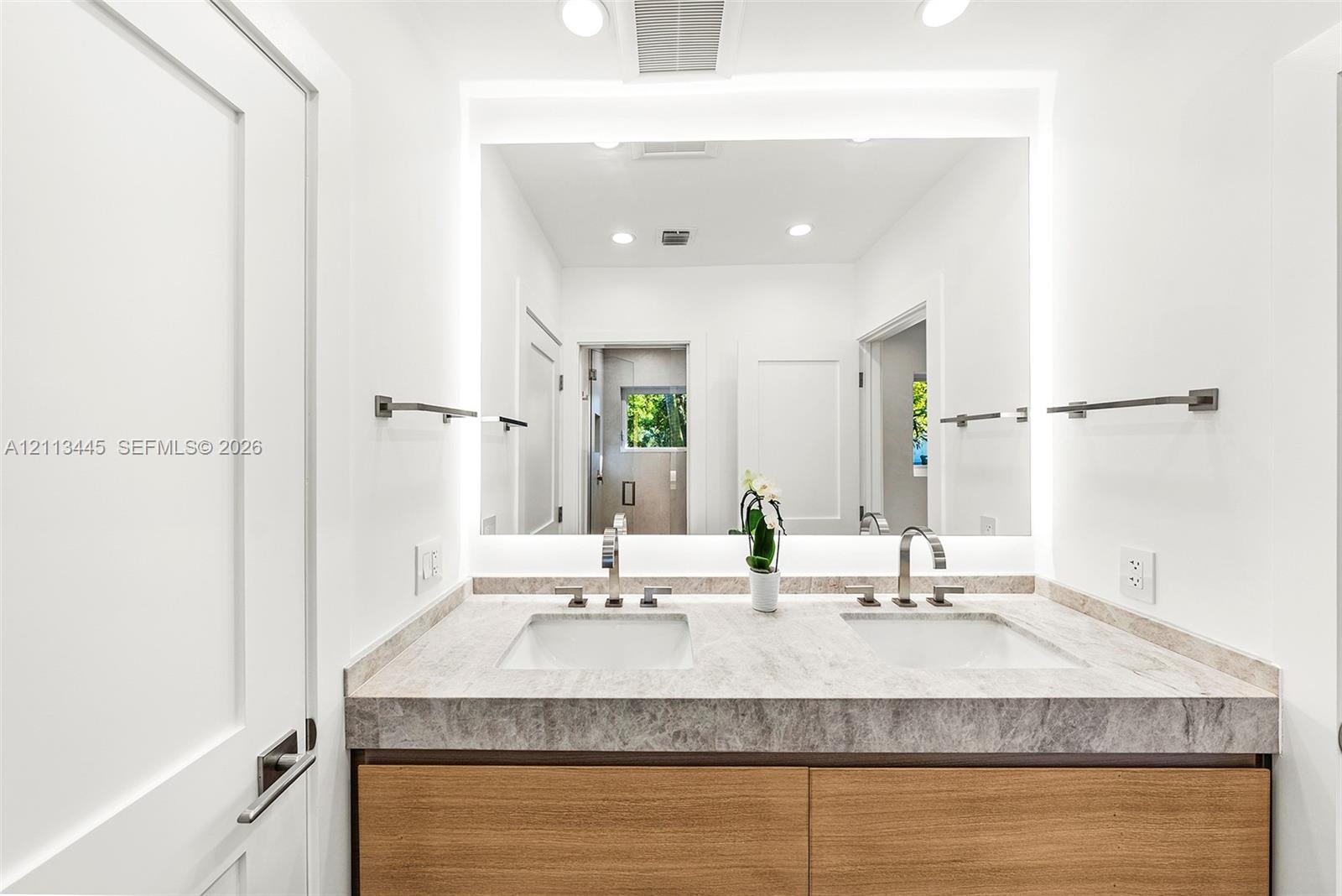 Dual-sink vanity featuring stone-finish countertop, wood-finish cabinetry, under-mount sinks, and wall-to-wall integrated backlighting