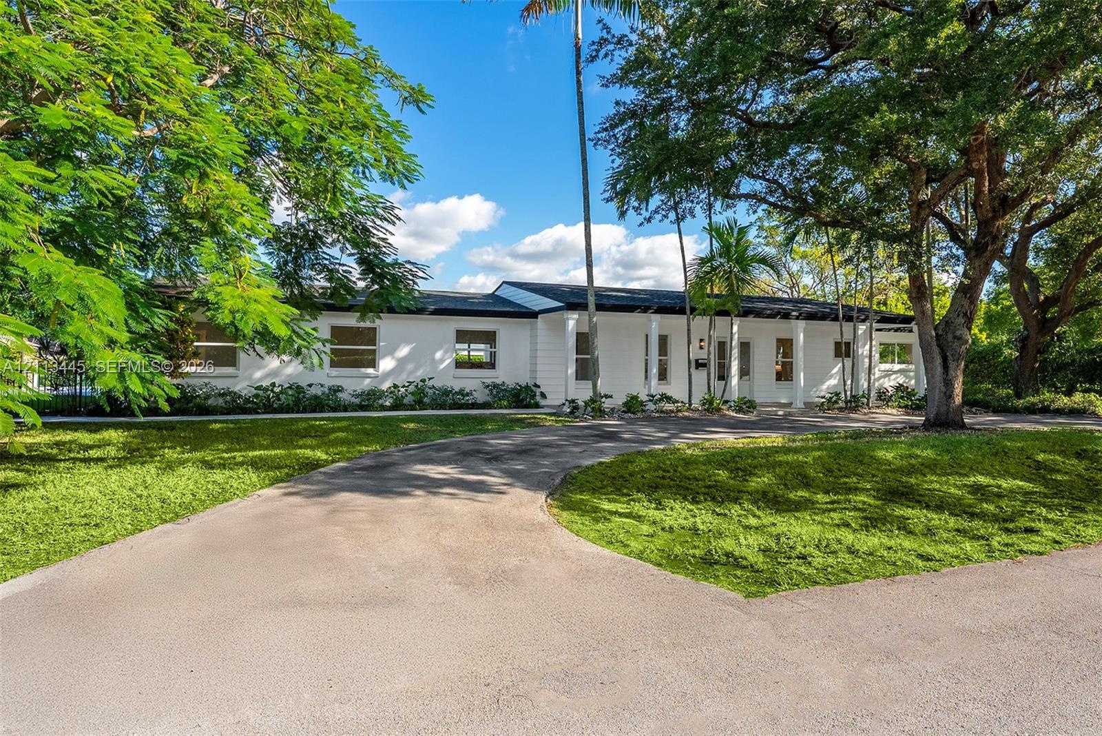 Single-story residence featuring a painted masonry exterior, covered entryway with structural columns, and a paved driveway, set upon a lot with matur
