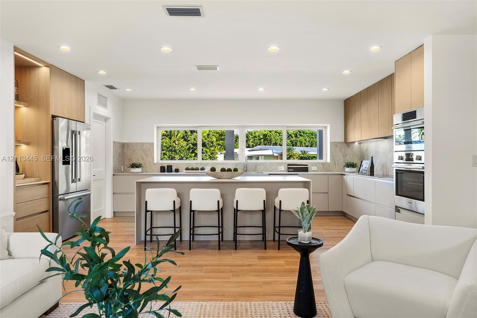 Modern kitchen featuring light wood-finish cabinetry, a central island with a solid-surface countertop, stainless steel appliances, stone-look backspl
