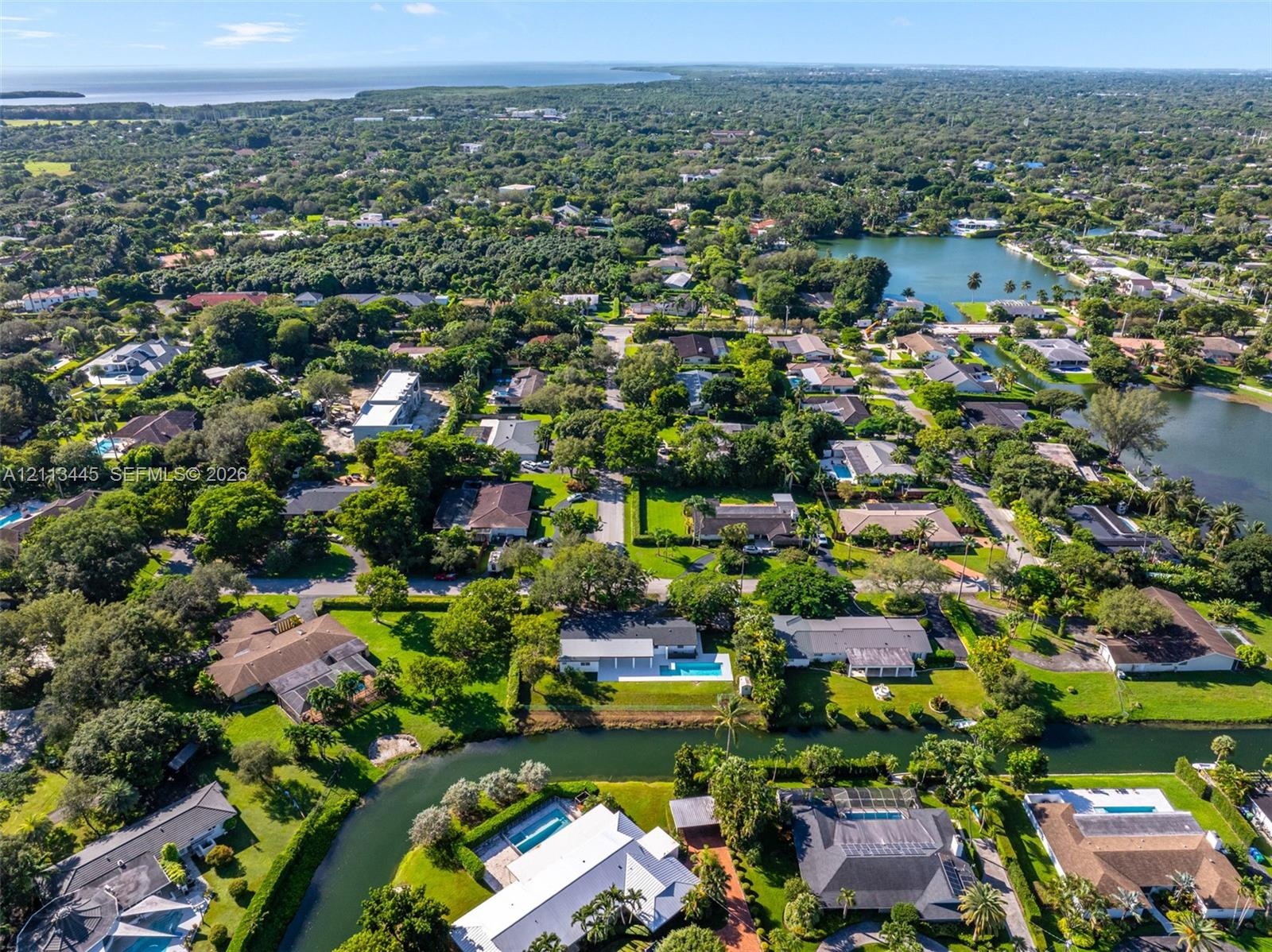 Aerial perspective featuring waterfront residential properties, mature tree canopy, integrated canal systems, and proximity to the coastline